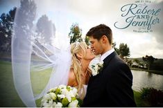 a bride and groom kissing in front of a lake with their veil blowing in the wind