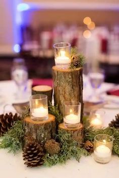 candles are placed on top of logs with pine cones and greenery in the center