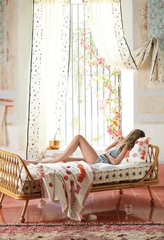 a woman is laying on a bed in front of a window with curtains and flowers