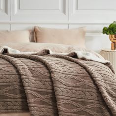 a bed with a blanket and pillows on top of it next to a vase filled with flowers