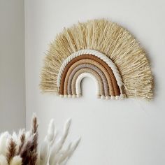 a wall hanging made out of straw with a rainbow in the middle and a plant next to it