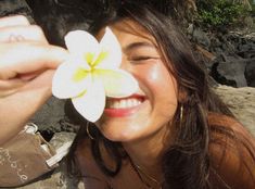 a woman is smiling and holding a flower in front of her face while she looks at the camera