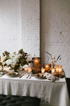 a table topped with lots of candles and plates filled with food next to white flowers