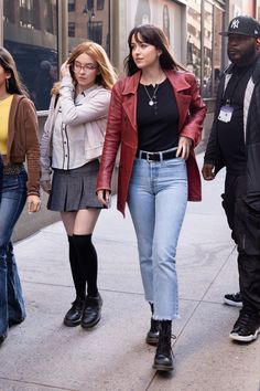 three women walking down the street in front of a man wearing a red leather jacket