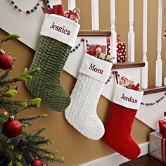 three christmas stockings hanging on the wall next to a stair case with personalized names