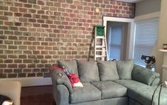 a living room filled with furniture and a brick wall behind the couches is a ladder