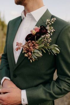 a man wearing a green suit and flower boutonniere with his hands in his pockets