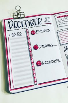 an open planner with the words december written in red and black on it, sitting on a white surface