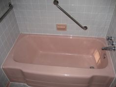 a pink bath tub sitting in a bathroom next to a shower head and hand rail