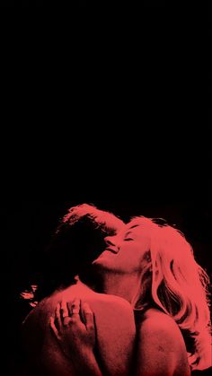 a man and woman kissing in the dark with red light on their faces, behind them is a black background