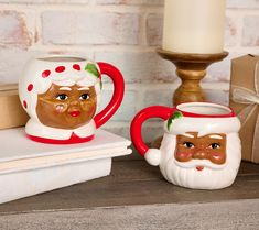 two coffee mugs with faces on them are sitting next to a candle and some books