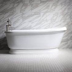 a white bath tub sitting on top of a bathroom floor next to a tiled wall