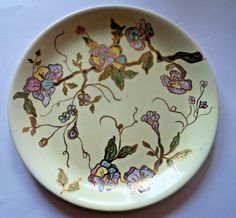 a plate with flowers painted on it sitting on a white tablecloth covered table top