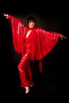 a woman in red is posing with her arms out and legs spread wide, wearing shiny clothing