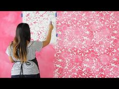 a woman is painting a pink wall with white flowers