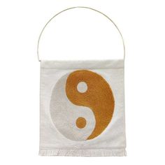 a white bag with an orange and white yin symbol on the front, hanging from a metal hook