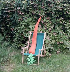 a lawn chair with an orange pillow on it in front of a bush and shrubbery