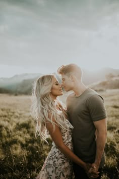 a man and woman are standing in the grass looking into each other's eyes