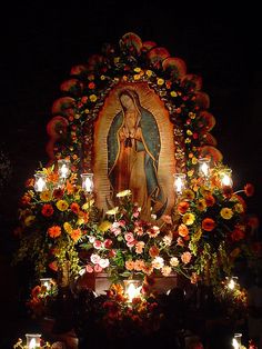 an image of the virgin mary surrounded by flowers and candles in front of a shrine