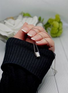 a woman's hand with white nail polish holding a silver chain bracelet and flower