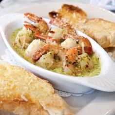 a white plate topped with bread and shrimp next to broccoli sauce in a bowl