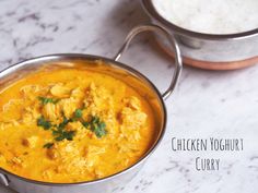 chicken yoghurt curry in a silver pot next to a white rice dish on a marble countertop