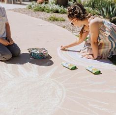 two children are drawing on the ground with chalk and paint while one child is sitting down