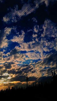 the sky is filled with clouds and power lines as the sun sets in the distance