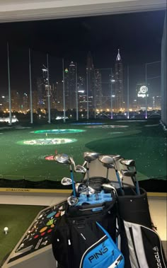 golf bags and clubs are sitting in front of a window overlooking the city skyline at night