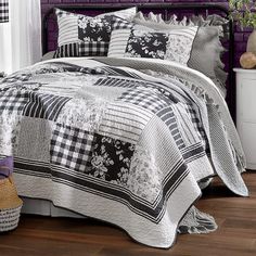 a bed covered in black and white quilts next to a purple headboard with flowers on it