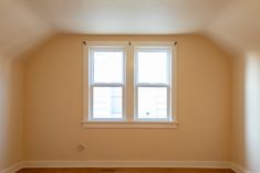 an empty room with two windows and hard wood flooring on the far wall,