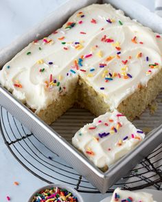 a cake with white frosting and sprinkles in a pan on a cooling rack