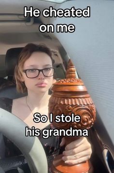 a woman sitting in the driver seat of a car holding a vase with words written on it