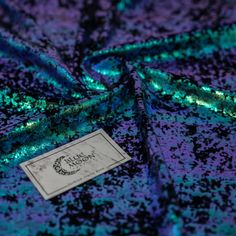 a purple and green sequinized fabric with a tag on it's side