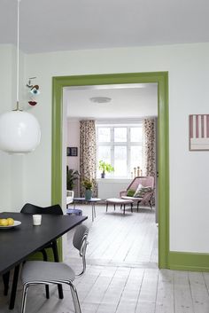 an open door leading to a living room and dining area with green trim on the walls