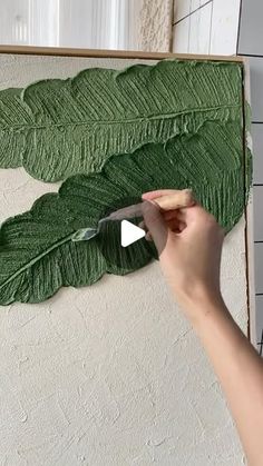 a person is using a knife to cut out leaves on a piece of green paper