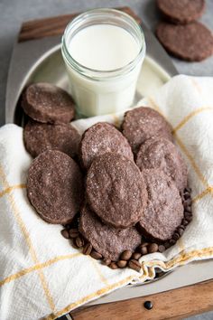 chocolate cookies on a plate with coffee beans and a glass of milk next to it