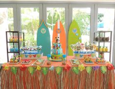 a table topped with lots of cakes and desserts next to surfboards on display