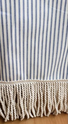 a blue and white striped curtain with tassels on the bottom, in front of a wooden floor