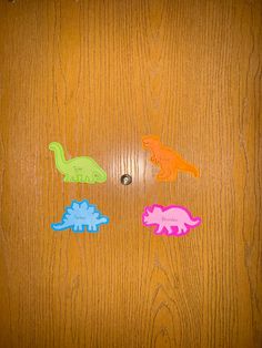 three different colored dinosaurs on a wooden surface