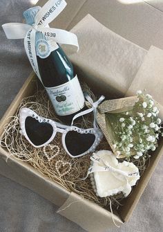 a bottle of wine and some sunglasses in a box on a bed with white flowers