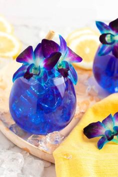 two blue vases filled with purple flowers sitting on top of a wooden tray next to lemon slices