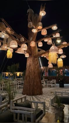 a large tree with many lights hanging from it's branches in the middle of an outdoor area