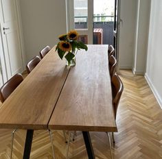 a wooden table with chairs and a vase filled with sunflowers sitting on top of it