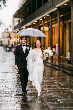 a bride and groom walking down the street under an umbrella