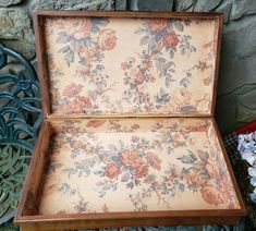 an old wooden box with floral designs on the outside and inside, sitting in front of a stone wall