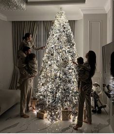 three people standing around a white christmas tree