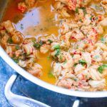 a pot filled with meat and vegetables on top of a blue stovetop next to a wooden spoon