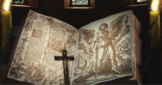 an open book with a cross on it in front of stained glass windows and candles