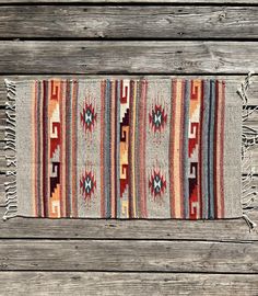 a multicolored rug with fringes on top of wooden planks in front of a wall